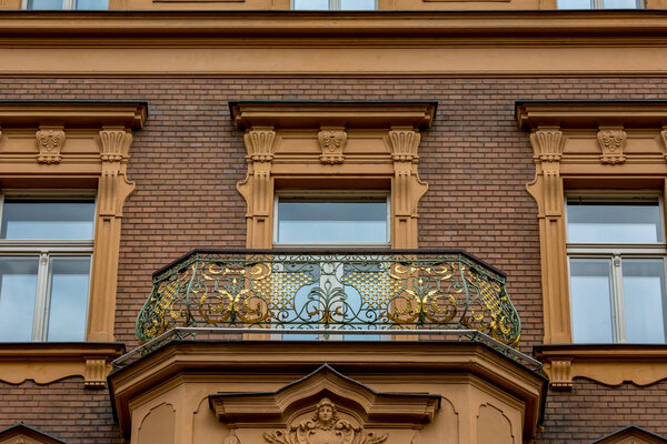 Amazing artistic architectural details of a residential building with gilded decorated balcony in the old center of Prague, Czech Republic, cloudy sky summer day cityscape close-up, two birds flying