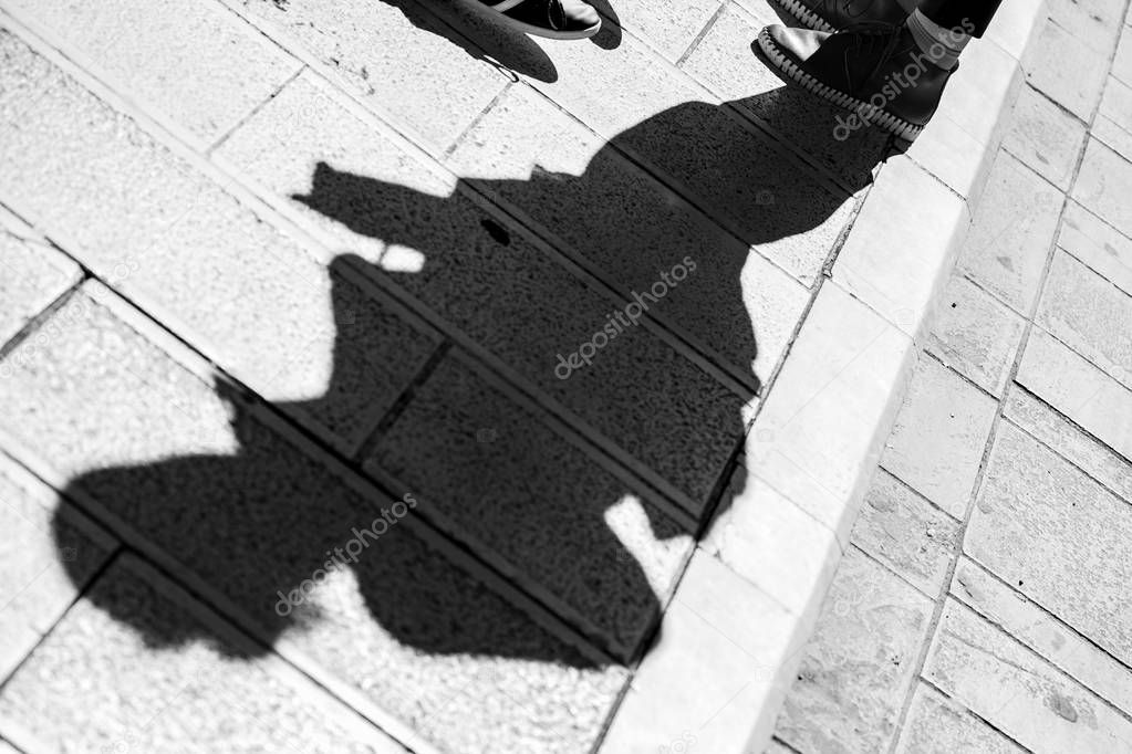 Diagonally composed photo of the shadow of one man with sporty shoes standing on a stone patio in the city of Corfu in Greece, black and white