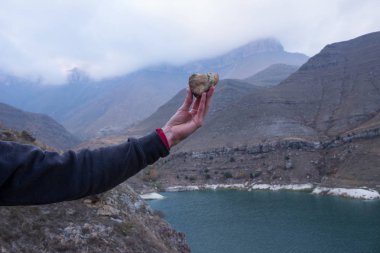 kalp şeklinde bir taş bir dağ manzarası karşı tutan bir erkek eli