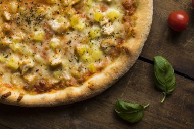 Klasik ahşap bir yüzey üzerinde ananas ve tavuklu bir pizza.