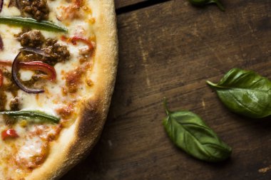 Eski bir ahşap yüzeyde fesleğen yapraklı kıymalı pizza.