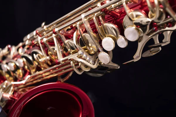 A red lacquered saxophone with gold plated keys on a black background