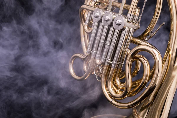 A part of a lacquered French horn in smoke on a black background