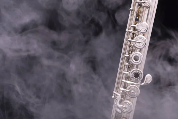 A silver plated flute in smoke on a black background