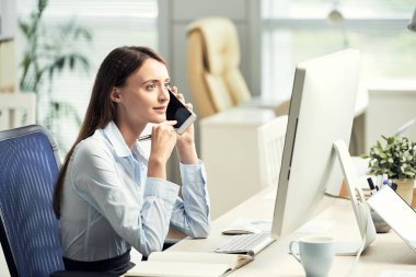 Çalışma masası oturma ve smartphone üzerinde konuşurken resmi kıyafeti genç kadın