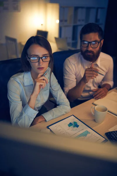 man and woman in glasses sitting at table in office and watching on computer monitor