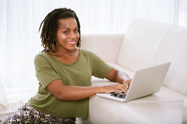 Katta, kanepe ve kameraya bakarak otururken dizüstü evde çalışan neşeli kadın portresi