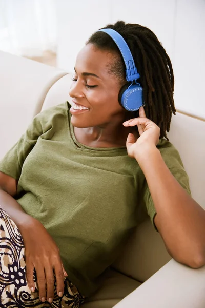 可爱的微笑的年轻妇女享受音乐在耳机和坐在沙发在家 — 图库照片