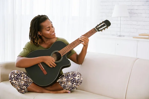 微笑的非洲裔美国妇女坐在沙发上弹吉他 — 图库照片