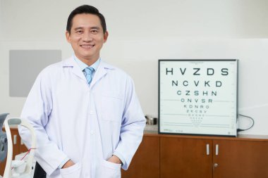 Doktor Oftalmoloji dolapta duran üniformalı neşeli Asyalı Doktor erkeklere 