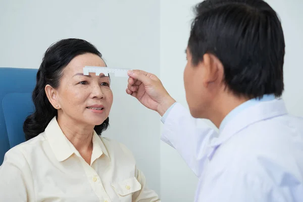 プロの Oculist 特別な定規を使用して キャビネットの病院で成熟したアジアの女性の目を測定 — ストック写真