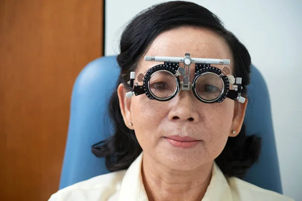 成熟的严肃的亚洲妇女在特别诊断眼镜与审判透镜在眼科看照相机的内阁 — 图库照片