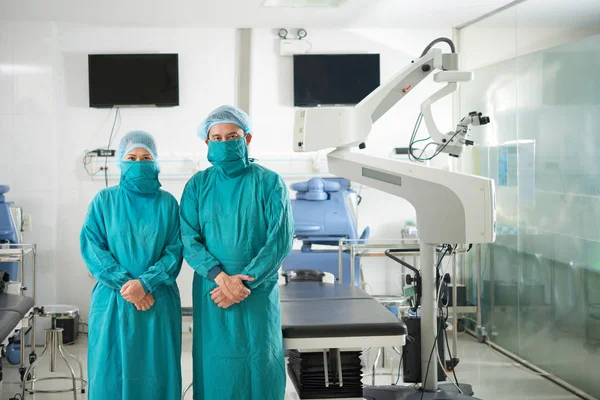 Asian doctors in green coats and masks standing in operation room