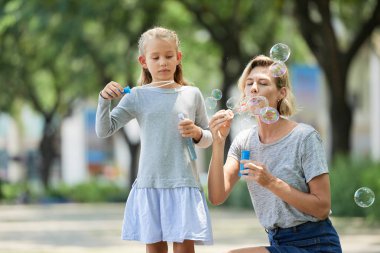 Anne ve kızı sabun köpüğü birlikte yaz parkta üfleme