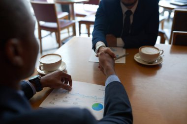 Masada cappuccino kupaları ve kağıtları ile el sıkışan iş ortakları 