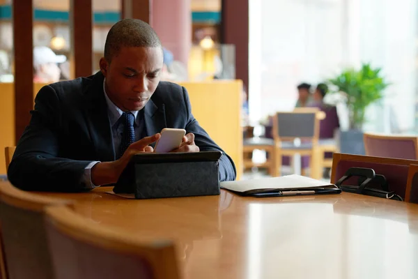 严肃的非洲裔美国商人阅读手机上的信息与数字平板电脑表 — 图库照片