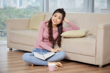 Güzel genç Vietnamlı öğrenci çay bardağı ve kitap ile katta oturan 