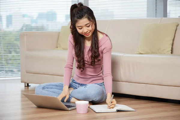 越南学生女孩在家做家庭作业 坐在地板上用笔记本电脑 课本和茶杯 — 图库照片