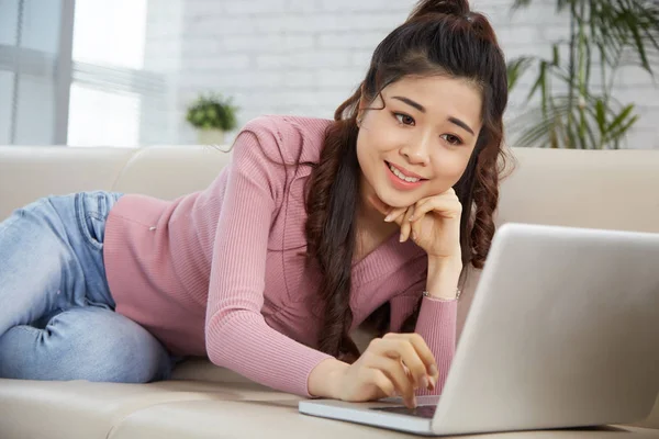 Vrij Lachende Aziatische Vrouw Liggend Bank Met Laptop — Stockfoto