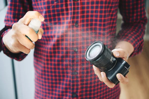 Cropped image man spraying on lens of photo camera with special cleaning fluid