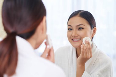 Gülümseyen genç ve güzel kadın makyaj pamuk yastık üzerinde micellar su ile kaldırma