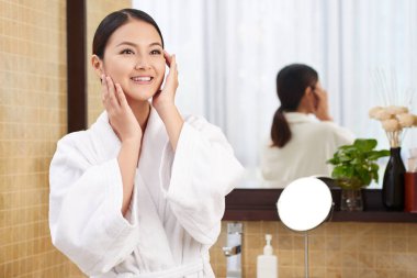 Gülümseyen ve nemlendirici yüzünü uygulayarak genç ve güzel Asyalı kadın