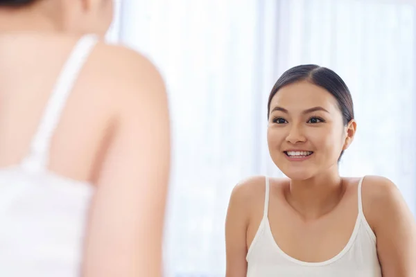 彼女はバスルームの鏡を見て幸せな美しい若いアジア女性 — ストック写真