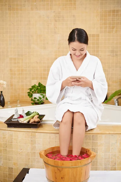 Vrouw Texting Zittend Met Voeten Houten Bekken Met Rozenblaadjes — Stockfoto