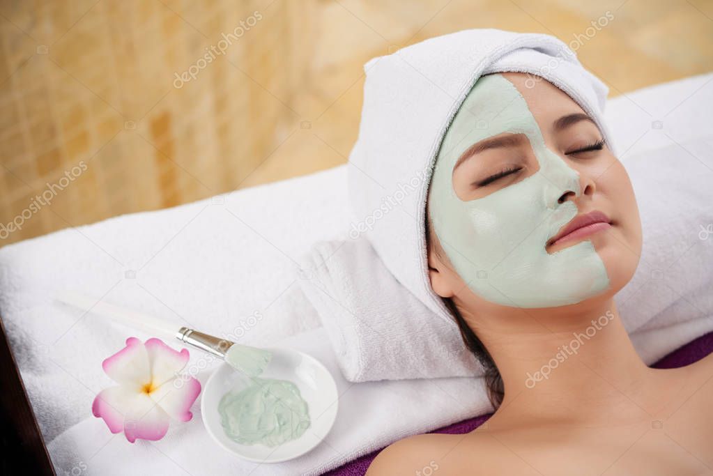 Beautiful Asian young woman lying with clay mask on half on her face