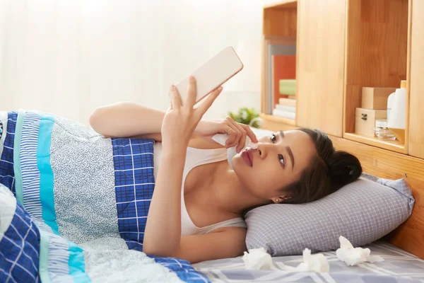 病気のベトナム人女性のベッドで横になっていると 彼女の携帯電話でニュースを読む — ストック写真