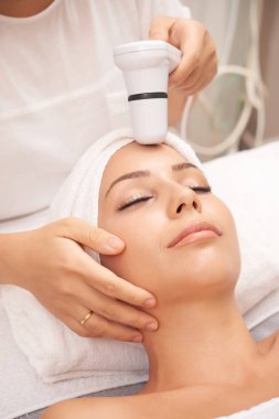 Modern beautician carrying out spa skincare procedure with special electric device clipart