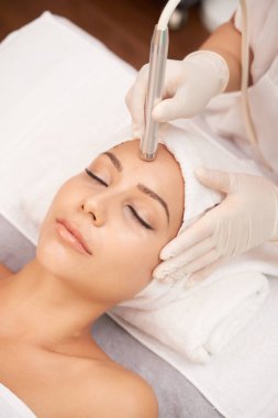 Relaxed woman lying in beauty salon and having anti-wrinkle therapy on her forehead clipart