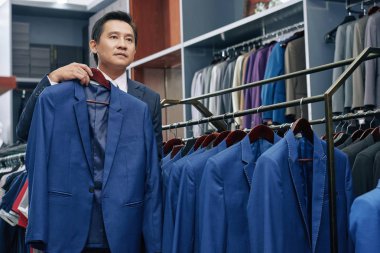 Takım elbise deposuna ayna önünde üzerinde çalışan orta yaşlı Vietnamca adam