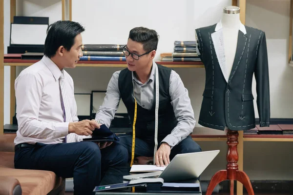 Mature Vietnamese man choosing fabric for the suit at tailors studio