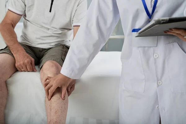 Doctor palpating leg of man after injury