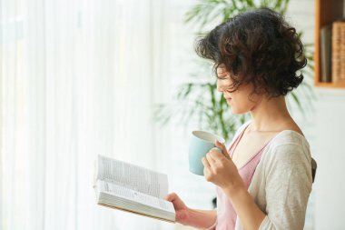 Kitap okuma ve çay bardağı tutan Asyalı kadın 