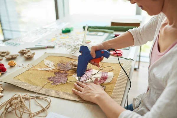 creative woman using hot glue gun while decorating textile picture with twine