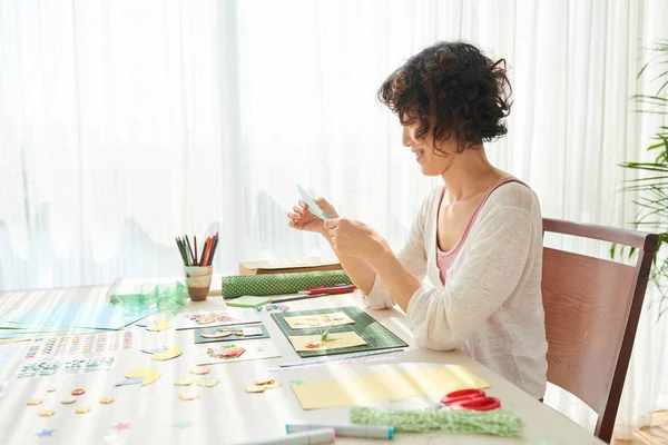 Ahşap masada oturan ve tebrik kartı yapmak neşeli Asyalı kadın profil görünümü