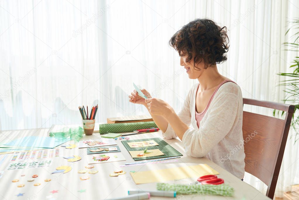 Profile view of cheerful asian woman sitting at wooden table and making greeting card
