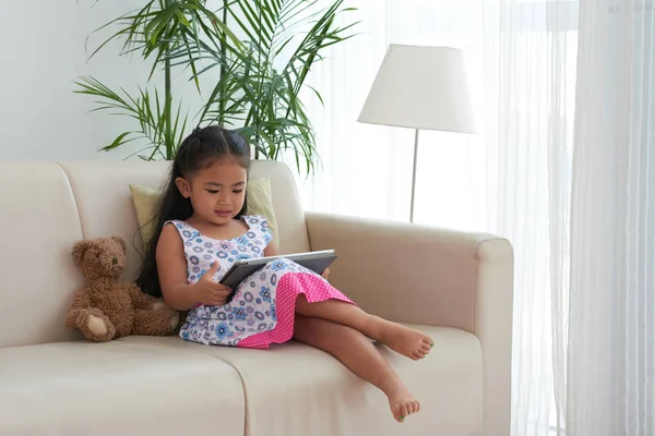 Μικρό Κορίτσι Που Κάθεται Στον Καναπέ Ψηφιακό Tablet Στα Γόνατα — Φωτογραφία Αρχείου