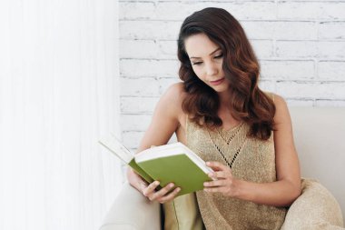 kitap okuma ve koltukta oturan dalgalı saçlı kadın 