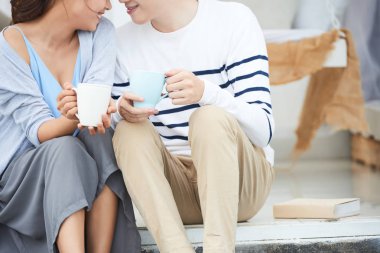 Kahve bardakları ile merdivenlerde oturan genç çift kırpılmış