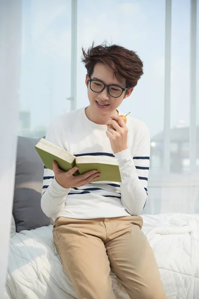 笑みを浮かべてベトナム人の若者男は梨を食べて 本を読んで — ストック写真
