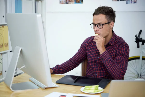 食べる青年実業家薄切りリンゴ作業オフィスでテーブルでコンピューターで作業 — ストック写真