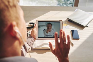Ofiste tablet meslektaşı ile bir video konferans olan işadamı 