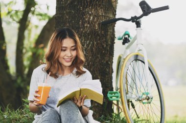 Gülümseyen güzel kadın içme güler yüzlü lezzetli ve ağacın altında bir kitap okuma