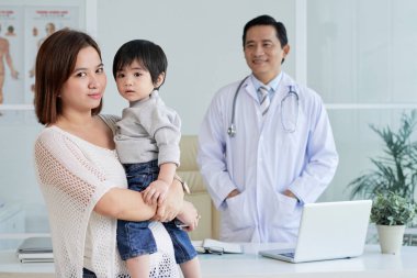 Asyalı kadın küçük oğlu üzerinde doktor ofisinde danışmanlık yaparken elele