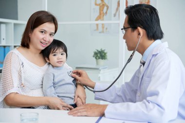 Doktor stetoskop kullanarak giyen beyaz önlük ve biraz sabırlı, annesini kameraya bakarak inceleyin