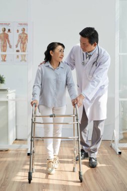 asian doctor helping senior patient to use front-wheeled walker  clipart