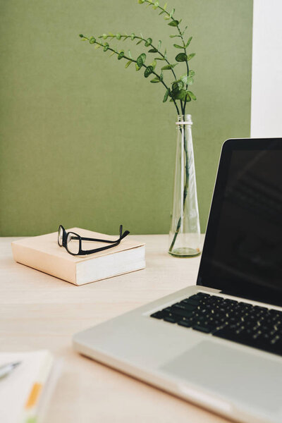 Opened laptop, book and glasses on table 